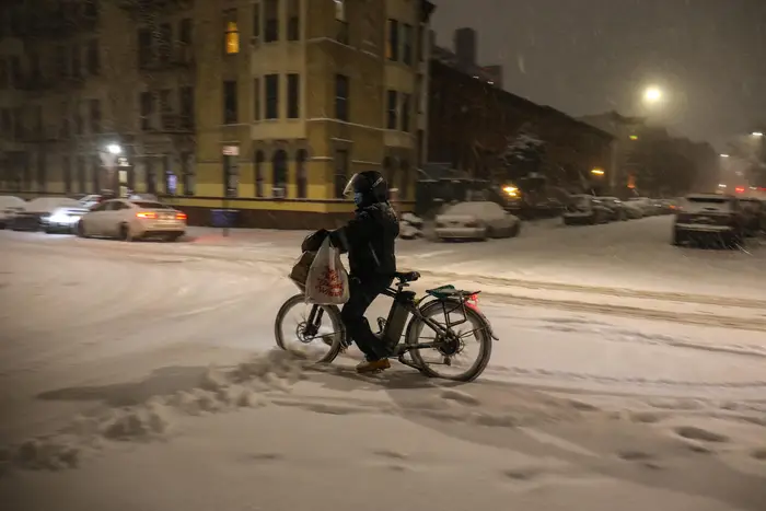 A food delivery worker on a bicycle navigates a snowy street now on the night of Dec 16th in Brooklyn.